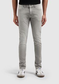Lichtgrijze slim-fit jeans met een gladde textuur, vijf-pocket ontwerp en een metalen knoopsluiting, geshowd met witte en grijze sneakers.