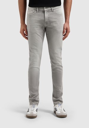 Lichtgrijze slim-fit jeans met een gladde textuur, vijf-pocket ontwerp en een metalen knoopsluiting, geshowd met witte en grijze sneakers.