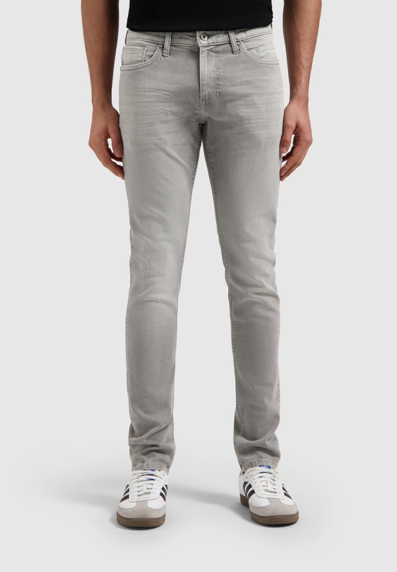 Lichtgrijze slim-fit jeans met een gladde textuur, vijf-pocket ontwerp en een metalen knoopsluiting, geshowd met witte en grijze sneakers.