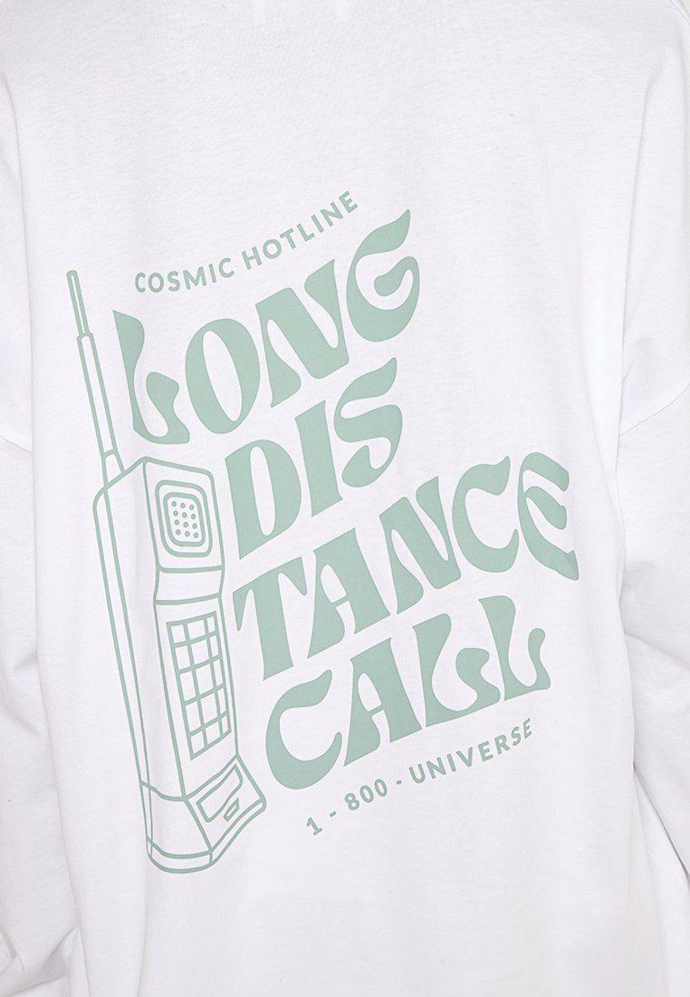 Weißes T-Shirt aus Stoff mit grüner Grafikschrift "LONG DISTANCE CALL" und einer Illustration eines Retro-Handys sowie "COSMIC HOTLINE 1-800-UNIVERSE."