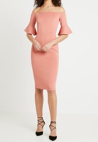 Off-shoulder rosa midiklänning med utställda ärmar, figursydd design, elastiskt tyg och rundad nederkant, tillsammans med svarta klackar med remmar.