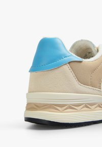 Beige sneaker with a textured suede and fabric upper, blue leather accent on heel, and a patterned light brown outsole.