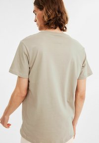 Beige bomulds t-shirt med rund hals og korte ærmer, der har en glat tekstur og et simpelt design. Den bageste udsigt viser minimal syning.