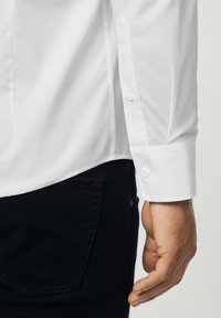Witte katoenen shirt met lange mouwen, voorzien van knoopmanchetten. Gepaard met zwarte denim jeans, met een gladde textuur en een aansluitend ontwerp.