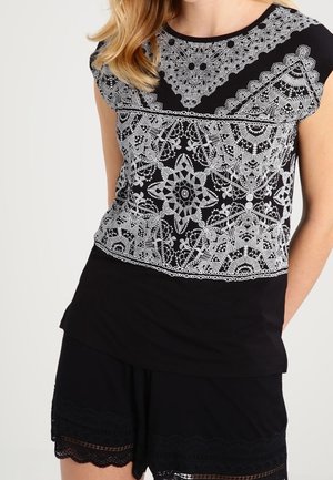 Czarna bluzka z białym, koronkowym wzorem i okrągłymi akcentami; miękki materiał; zestawiona z czarnymi szortami ozdobionymi koronkową lamówką na dole.