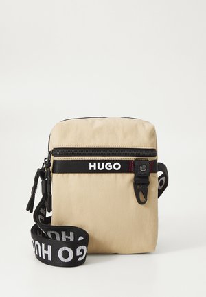 Borsa a tracolla in tessuto beige con una tracolla nera, caratterizzata dal logo "HUGO", chiusura con zip e una superficie testurizzata con cuciture a contrasto rosse.