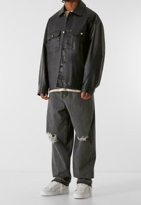 Czarna skórzana kurtka z buttonem z przodu, dwoma kieszeniami na piersi i klasycznym kołnierzykiem. W zestawie z przetartymi, oversize'owymi szarymi dżinsami i białymi sneakersami.