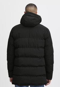 Chaqueta de plumas negra con capucha, que presenta un diseño acolchado y costuras visibles. El material parece suave con un acabado mate.