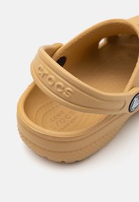 Bruna gummitofflor från Crocs med bred rem, prydda med ett präglat märke och strukturerad innersula, designade för komfort och andningsförmåga.