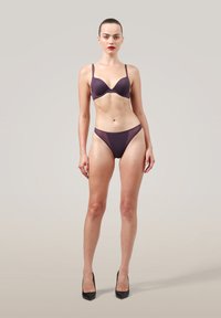 Trådlös lila bh med justerbara band, matchad med lila stringtrosa. Slät textur; minimalistisk design. Hög midja.