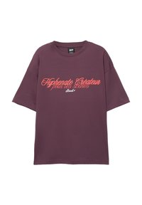 Bordeaux oversized t-shirt lavet af bomuld, med korte ærmer og rund halsudskæring. Text trykt i kontrasterende koralfarvet skrift på forsiden.