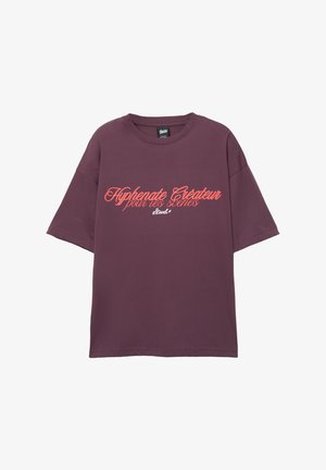 T-shirt oversize bordeaux en coton, avec des manches courtes et un col rond. Texte imprimé en calligraphie corail contrastante sur le devant.