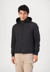Black padded jacket with a glossy hood, zip closure, and logo accents; features solid color and elastic cuffs. Casual design.