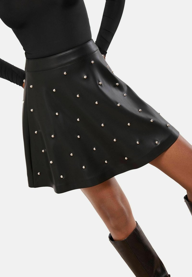 Fekete műbőr szoknya, fodros kivitelben, ezüst szegecsekkel díszítve, magas derékkal és sima textúrával.