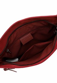 Red fabric bag interior with a zipped pocket and multiple compartments. Smooth texture, plain design with a branded leather label inside.