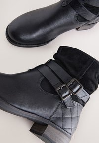 Black ankle boots with a textured leather upper and suede accents. Features double buckles and a low wooden heel.
