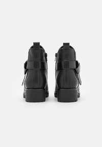 Bottines noires en simili cuir avec un panneau arrière texturé, une fermeture éclair latérale et une semelle épaisse. Présente des accents décoratifs de boucle.