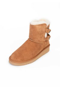 Stivaletti alla caviglia in suede beige con morbida foderatura in pelliccia bianca, punta arrotondata, bottoni laterali e suola piatta in gomma.