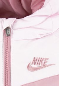 Rosa Nike-huvtröja med dragkedja, slät textur och subtilt broderad logotyp på bröstet.