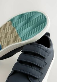 Námornícky modré tenisky s tromi čiernymi suchými zipsami, bielou gumovou podrážkou a textúrovanou teal a krémovou herringbone vzorovanou spodnou časťou.