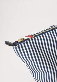 Pochette rayée bleu marine et blanche avec fermeture éclair dorée, ornée d'un tirette de fermeture éclair colorée. Matériau texturé avec une forme structurée.