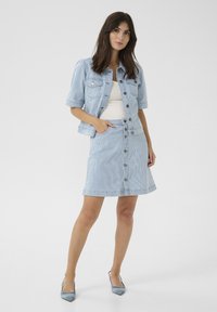 Világoskék farmerdzseki rövid ujjakkal, egy hozzáillő csíkozott szoknyával párosítva, amely elöl gombokkal záródik. Elegánsan illeszkedik a sziluetthez.