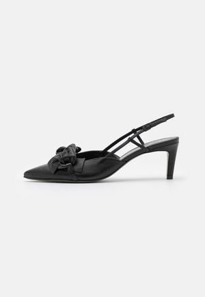 Tacón de espalda negro con punta afilada, que presenta un upper de cuero suave y un detalle decorativo de nudo en la parte frontal. Correa ajustable.