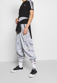 Svart t-shirt med kort ärm och vit logga, grå oversized cargo-byxor med fickor, svarta sneakers och vita strumpor med logga.