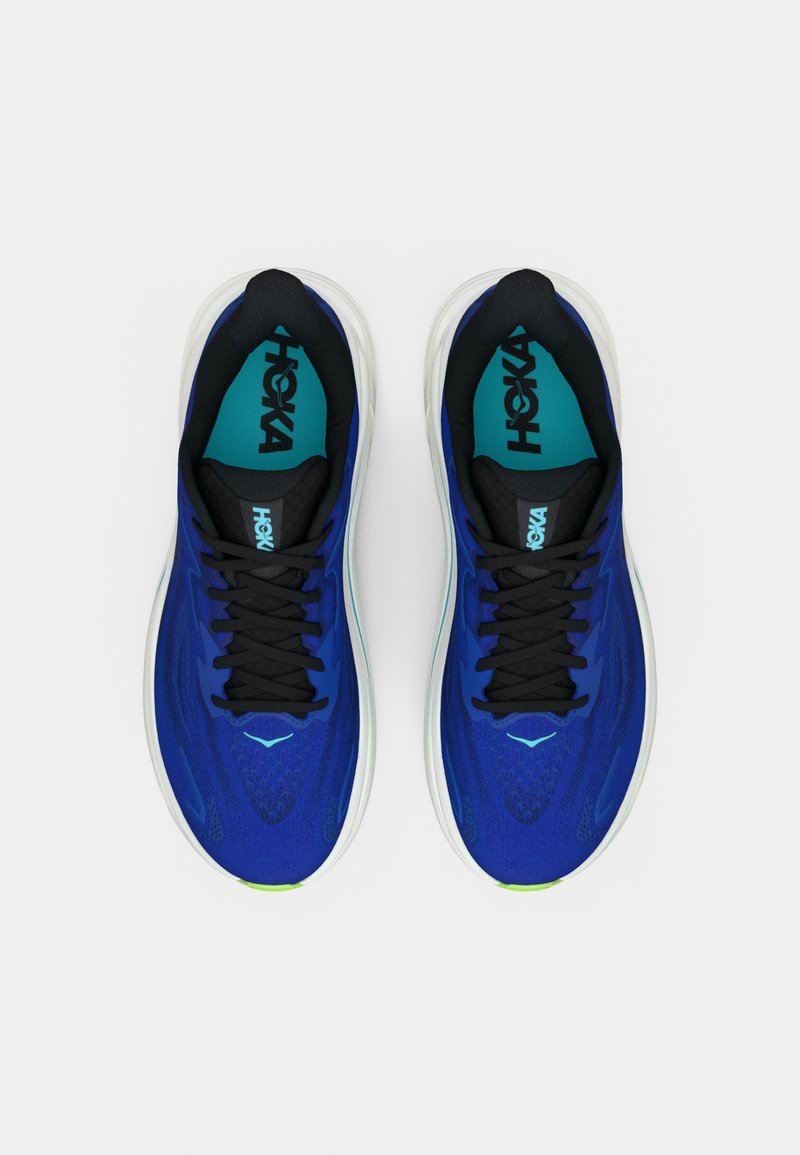 Ett par blå och svarta löparskor med vita sulor, turkosa innersulor och svarta snörning, fotograferat ovanifrån på en vit bakgrund.