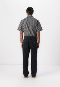 Black denim pants with straight legs, featuring two back pockets. Worn with a short-sleeve striped shirt in black and white.