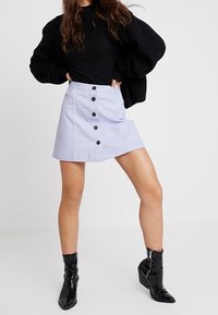 Ljuslila denimkjol med hög midja, som har en fem-knapsknäppning och en utsvängd nederdel. Parat med svarta, glänsande ankelboots.