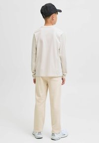 Beige overhemd met lange mouwen, crèmekleurige broek en zwarte pet. Eenvoudig ontwerp, zachte textuur. Witte sneakers met grijze accenten maken de outfit compleet.