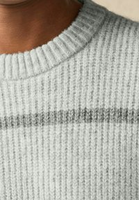 Grijze gebreide trui met een geribde halslijn. Heeft een lichtgrijze basis en een donkergrijze horizontale streep. Zachte textuur en warm ontwerp.