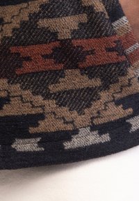 Gebreide stof met een geometrisch patroon in verschillende tinten bruin, zwart en grijs, met een gladde textuur en een contrasterende rode streepdetail.