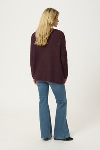 Maroon knitted sweater with a textured, loose fit. Paired with light blue flared jeans and black shoes. The sweater has a slightly longer back.