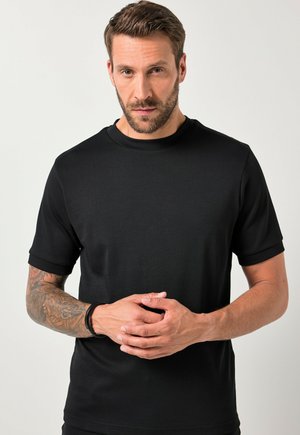 Zwarte katoenen t-shirt met korte mouwen en ronde hals, gladde textuur, getailleerde pasvorm en minimale details, gedragen door een man die met gekruiste handen staat.