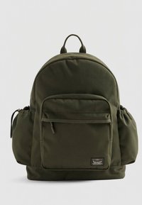 Batoh z olivově zelené látky zaobleného tvaru, s přední kapsou, elastickými bočními kapsami a horním madlem pro přenášení.