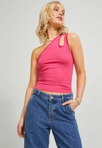 Top fucsia de un solo hombro hecho de tejido elástico; presenta un detalle de ojal en el hombro y se combina con jeans de mezclilla azules de cintura alta.