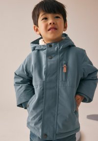 Niebieska kurtka z kapturem, ocieplona sherpa, z zatrzaskami oraz kieszenią na piersi z skórzanym uchwytem. Przytulny i odporny na warunki atmosferyczne design.