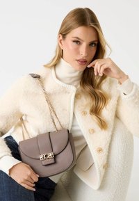 Szara torebka crossbody z ekologicznej skóry z metalowym zapięciem, złotym łańcuchem i zaokrąglonym klapem. Nosi się ją z kremową, fakturowaną kurtką i swetrem.