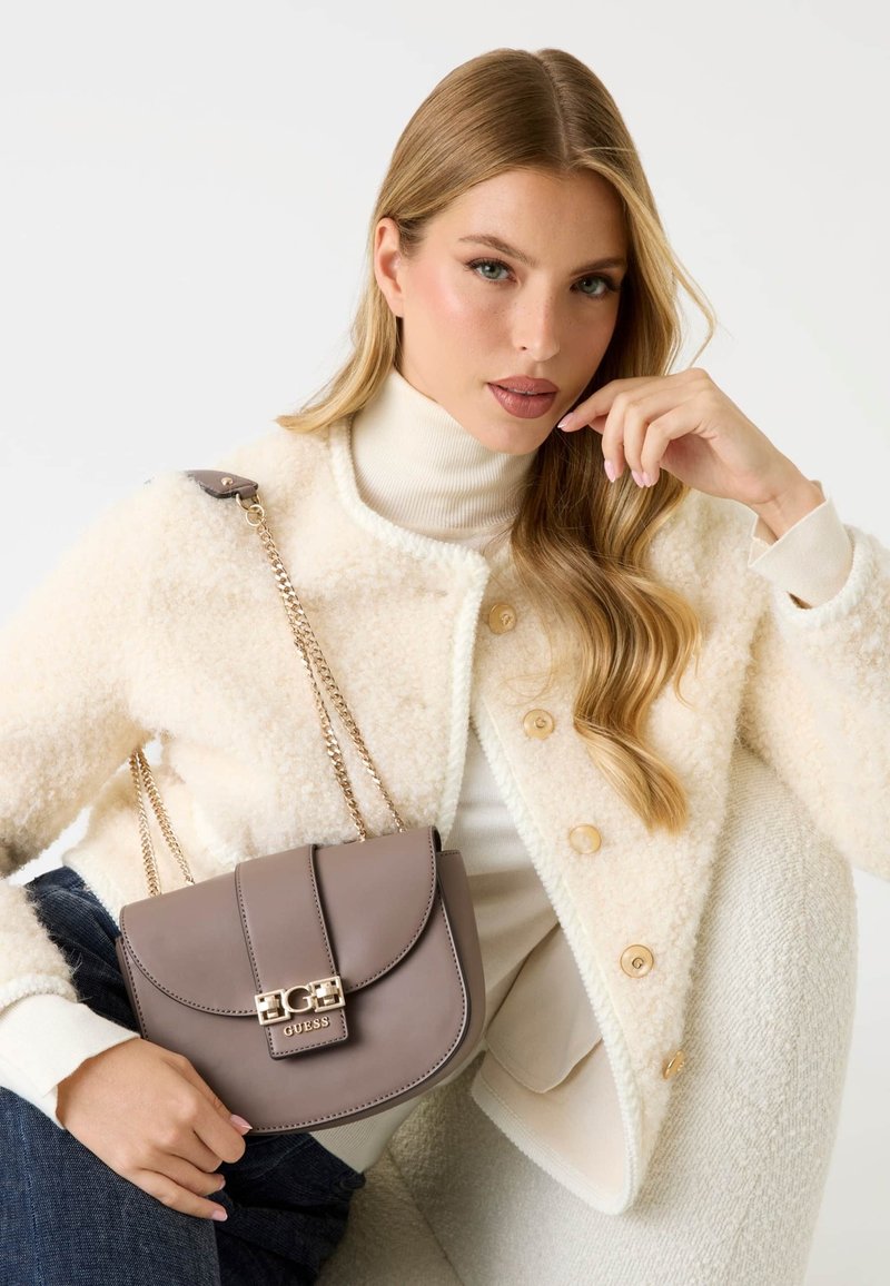 Szara torebka crossbody z ekologicznej skóry z metalowym zapięciem, złotym łańcuchem i zaokrąglonym klapem. Nosi się ją z kremową, fakturowaną kurtką i swetrem.