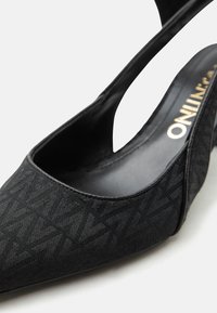 Μαύρη γόβα με μυτερή μύτη και κούμπωμα στο πίσω μέρος, με υφασμάτινο επάνω μέρος διακοσμημένο με επαναλαμβανόμενο μοτίβο "MAX" και ορατή επωνυμία μέσα στην εσωτερική σόλα.