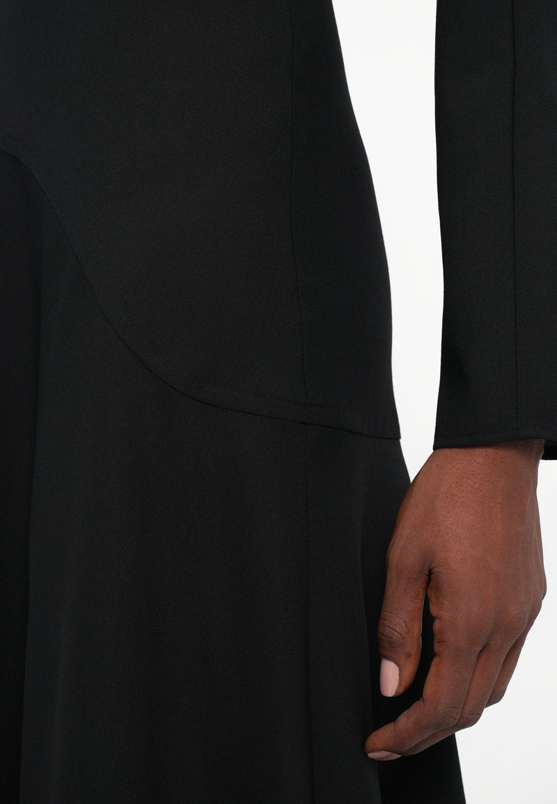 Main droite d'une personne à la peau foncée reposant à côté d'un vêtement noir ajusté avec des détails de couture visibles.