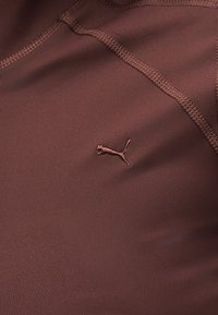 Κοντινή λήψη καφέ αθλητικού υφάσματος με κεντητό λογότυπο Puma και ορατές ραφές.