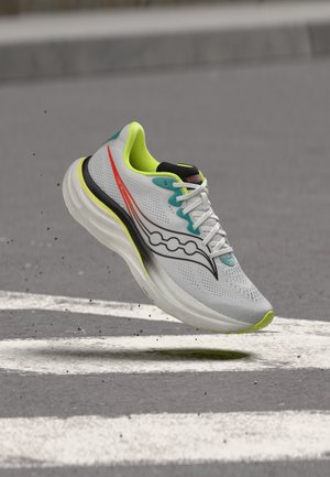 Chaussure de course gris clair avec des accents jaune néon et sarcelle et un logo noir, survolant une rue avec des marquages blancs peints.