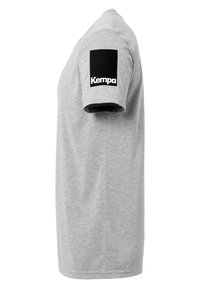 Grå bomulds-t-shirt med et sort mærke på venstre ærme med "Kempa" branding i hvid tekst. Casual, kortærmet design.