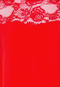 Tessuto rosso con motivo in pizzo floreale lungo il bordo superiore, caratterizzato da intricati disegni di rose e foglie.