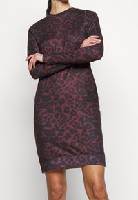 Leopardmönstrad tröjdress i mörkröd och svart. Långa ärmar, ribbad mudd och fåll. Mjuk stickad tyg med lös passform.