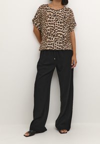 Blouse à manches courtes en imprimé léopard beige et marron, associée à un pantalon noir loose avec taille élastique et délicates petites garnitures dorées.