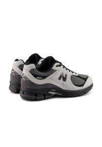 Γκρι και μαύρα αθλητικά παπούτσια με πλέγμα και συνθετικά υλικά, στρογγυλεμένη μύτη, μαλακή σόλα και εμφανές λογότυπο "N" στο πλάι.